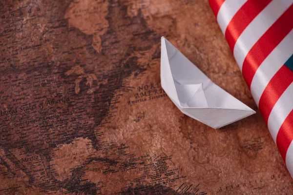 Barco de papel blanco cerca de bandera nacional estadounidense en el mapa del mundo antiguo - foto de stock