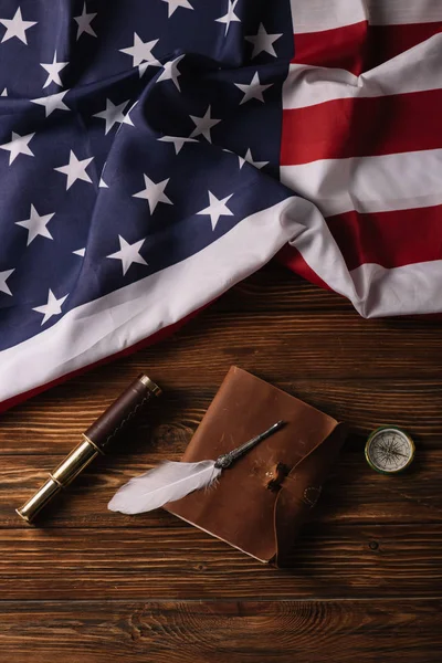 Top view of leather notebook, nib, telescope and compass on wooden surface with American national flag — Stock Photo