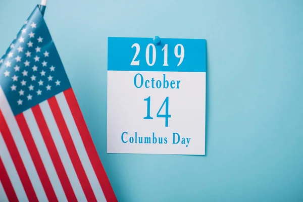 Calendario de papel con inscripción del Día de Colón cerca de la bandera nacional estadounidense sobre fondo azul - foto de stock