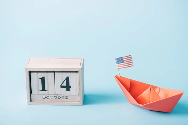 Calendario in legno con 14 ottobre data vicino cinghiale di carta rossa con bandiera americana su sfondo blu — Foto stock