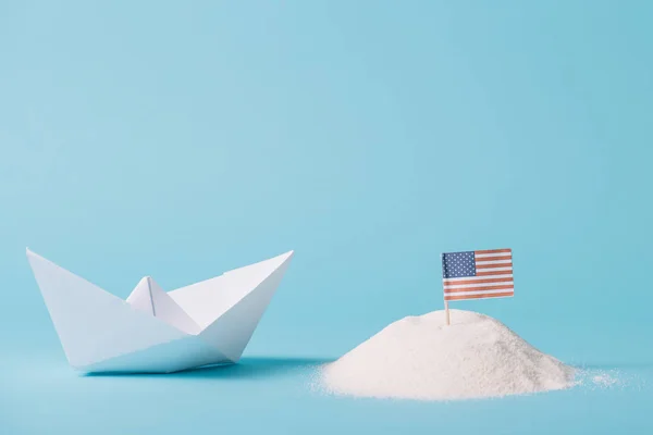 Paper boat near American national flag in white sand on blue background — Stock Photo