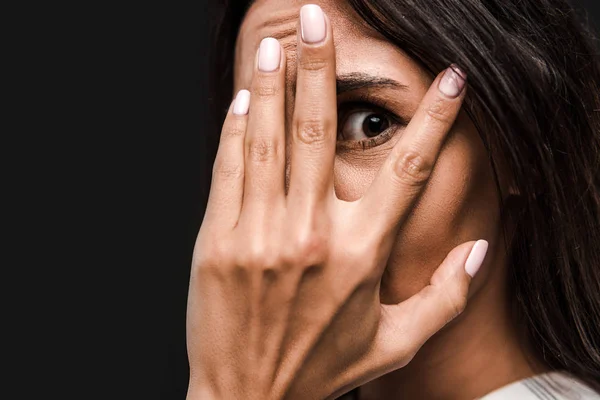 Assustado jovem mulher cobrindo rosto e olhando para câmera isolada no preto — Fotografia de Stock