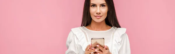 Plano panorámico de hermosa chica en vestido blanco sosteniendo teléfono inteligente aislado en rosa - foto de stock