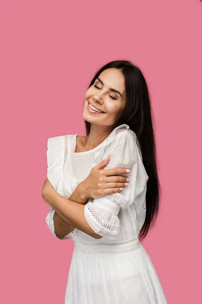 Mulher sorridente em vestido branco tocando corpo isolado em rosa — Fotografia de Stock