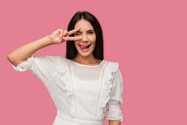 Happy woman in dress showing tongue and peace sign isolated on pink — Stock Photo