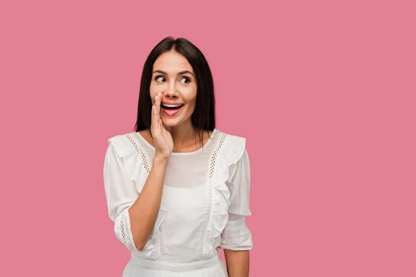 Cheerful woman touching face while gossiping isolated on pink — Stock Photo