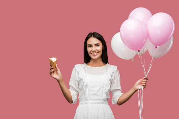 Cheerful girl in dress holding balloons and ice cream cone isolated on pink — Stock Photo