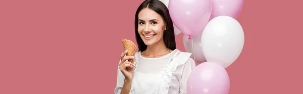 Panoramic shot of woman holding balloons and ice cream cone isolated on pink — Stock Photo