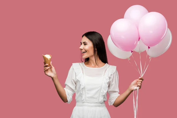 Excited woman holding balloons and looking at ice cream cone isolated on pink — Stock Photo