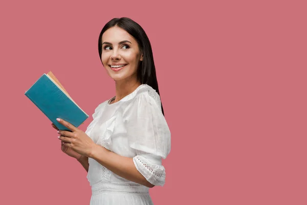 Happy young woman in dress holding book isolated on pink — Stock Photo