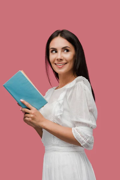 Alegre joven en vestido sosteniendo libro aislado en rosa - foto de stock