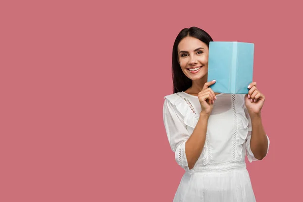 Весела молода жінка в одязі тримає синю книгу ізольовано на рожевому — стокове фото