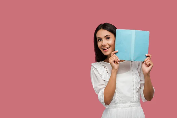 Positive jeune femme en robe tenant livre bleu isolé sur rose — Photo de stock