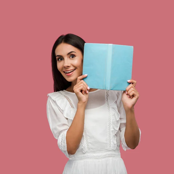 Mulher feliz em vestido branco segurando livro azul isolado em rosa — Fotografia de Stock