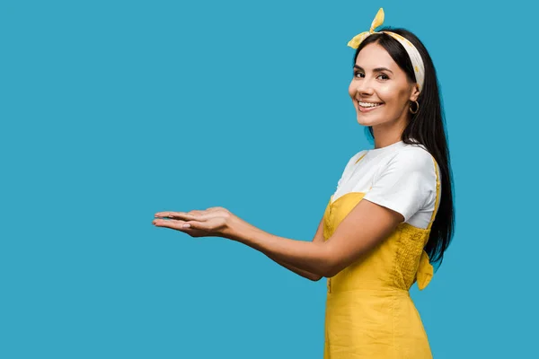 Fröhliche junge Frau mit Stirnband gestikuliert vereinzelt auf blauem Grund — Stockfoto