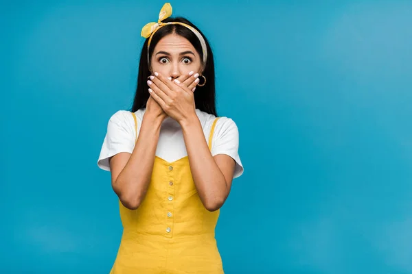 Scared woman in headband covering mouth isolated on blue — Stock Photo