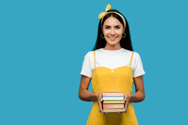 Glückliches Mädchen, das Bücher in der Hand hält und isoliert auf blau in die Kamera blickt — Stockfoto