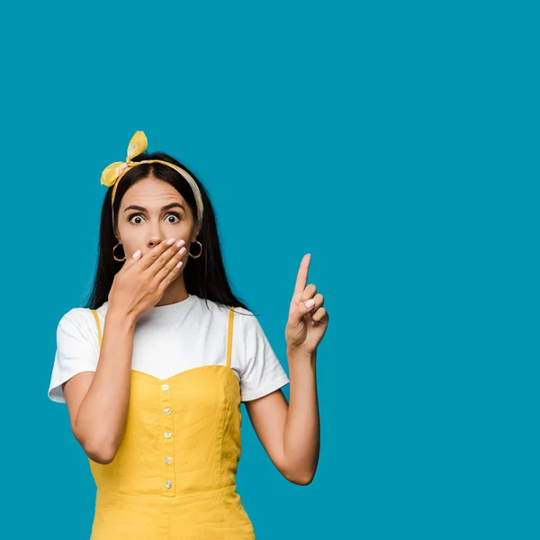 Mujer impactada cubriendo la boca mientras señala con el dedo aislado en azul - foto de stock