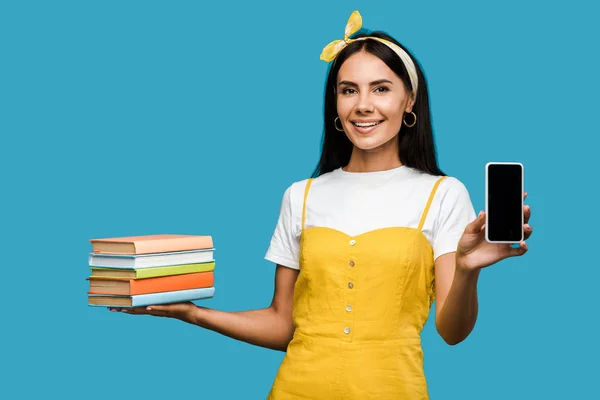 Femme positive tenant des livres et smartphone avec écran blanc isolé sur bleu — Photo de stock