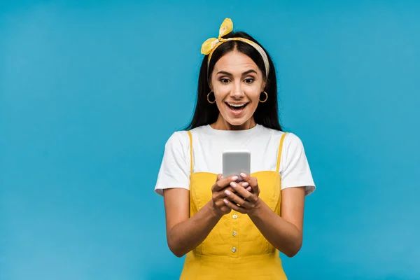 Enfoque selectivo de la mujer sorprendida mirando teléfono inteligente aislado en azul - foto de stock