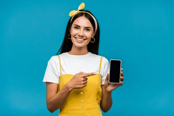 Glückliches Mädchen zeigt mit dem Finger auf Smartphone mit leerem Bildschirm isoliert auf blau — Stockfoto