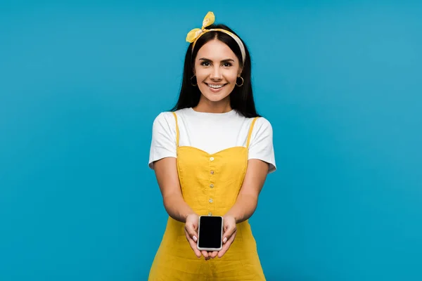 Glückliche Frau in gelbem Kleid hält Smartphone mit leerem Bildschirm isoliert auf blau — Stockfoto