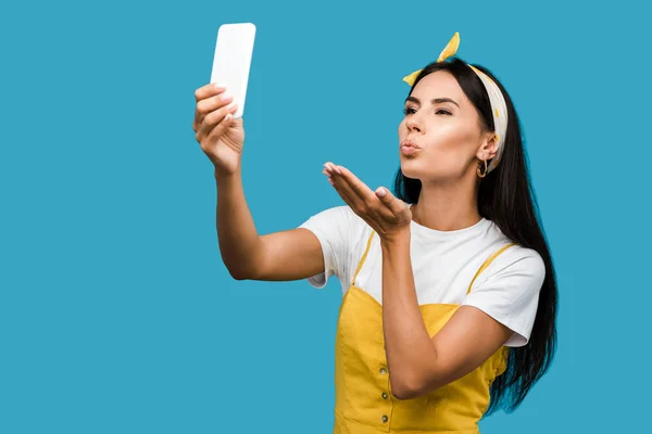 Молода жінка бере селфі на смартфон, відправляючи повітряний поцілунок ізольовано на синьому — стокове фото