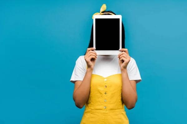 Joven mujer cubriendo la cara con tableta digital con pantalla en blanco aislado en azul - foto de stock