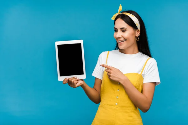 Chica feliz apuntando con el dedo a la tableta digital con pantalla en blanco aislado en azul - foto de stock