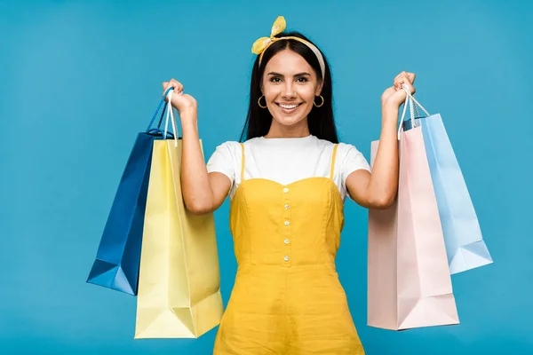 Feliz mujer joven sosteniendo coloridas bolsas de compras aisladas en azul - foto de stock