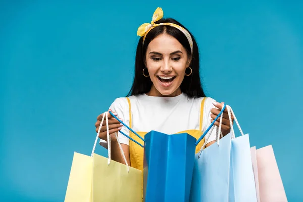Jovem feliz olhando para sacos de compras isolados em azul — Fotografia de Stock