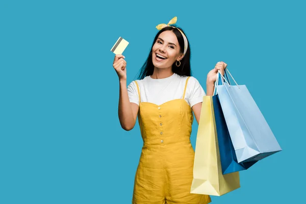 Feliz joven con tarjeta de crédito y bolsas de compras aisladas en azul - foto de stock