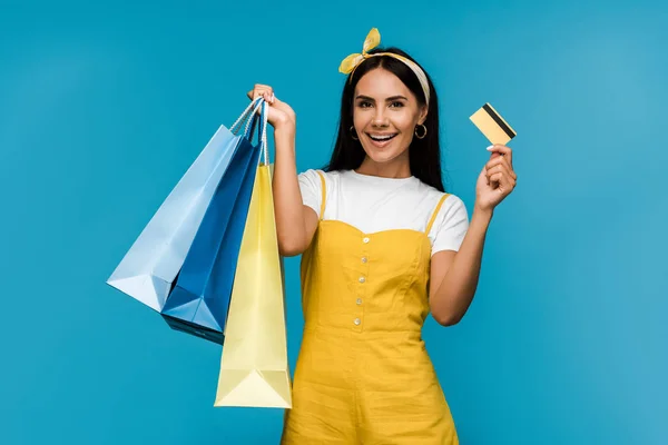 Fille heureuse tenant carte de crédit et sacs à provisions isolés sur bleu — Photo de stock