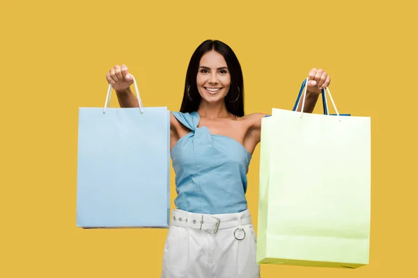 Happy young woman smiling while holding shopping bags isolated on orange — Stock Photo