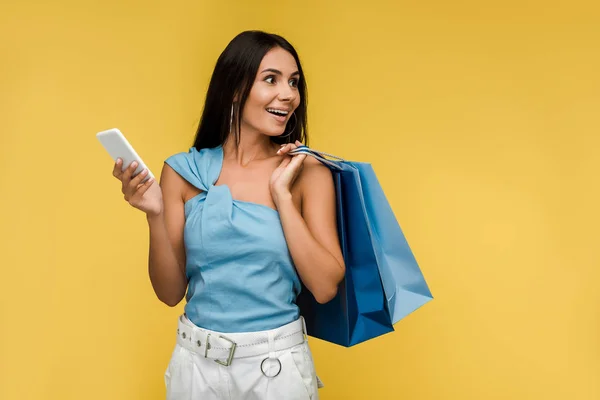 Excited woman holding smartphone with shopping bags isolated on orange — Stock Photo
