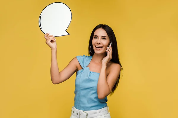 Cheerful girl holding blank speech bubble while talking on smartphone isolated on orange — Stock Photo