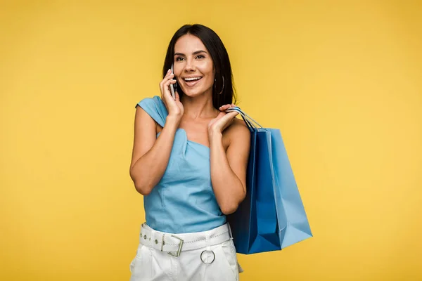 Happy woman holding shopping bags and talking on smartphone isolated on orange — Stock Photo
