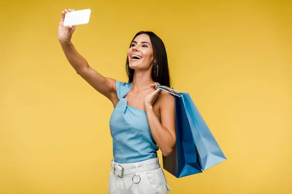 Mujer feliz sosteniendo bolsas de compras y tomando selfie en el teléfono inteligente en naranja - foto de stock