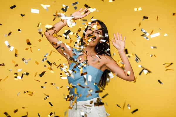 Selective focus of woman gesturing near falling confetti on orange — Stock Photo