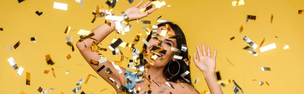 Panoramic shot of cheerful young woman gesturing near sparkling confetti on orange — Stock Photo