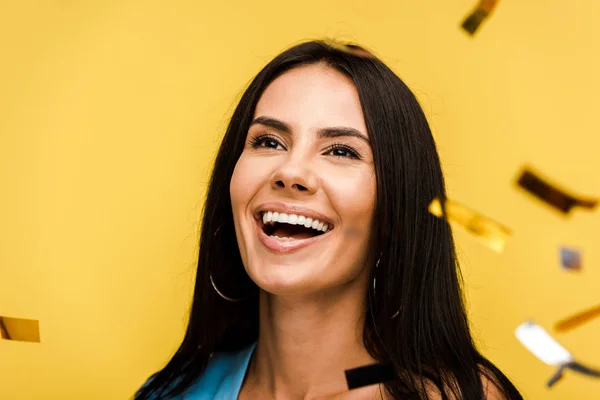 Selective focus of happy woman smiling near falling confetti on orange — Stock Photo