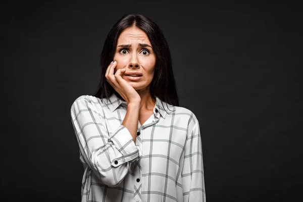 Scared woman looking at camera while touching face isolated on black — Stock Photo