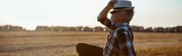 Panoramic shot of bearded farmer touching straw hat — Stock Photo