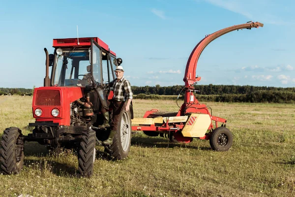 Agricultor senior en sombrero de paja cerca de tractor moderno - foto de stock