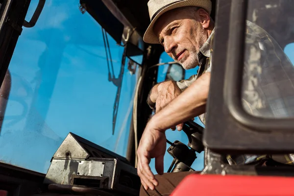 Blick in den niedrigen Winkel: Senior-Landwirt streift Lenkrad in Traktor — Stockfoto