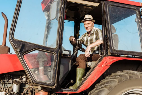 Happy senior self-employed farmer in straw hat driving tractor — Stock Photo