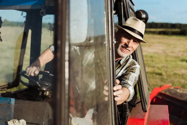 Selective focus of cheerful senior farmer driving tractor — Stock Photo