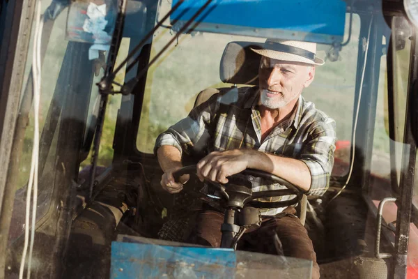 Вибірковий фокус веселого самозайнятого фермера, який посміхається під час руху трактора — стокове фото