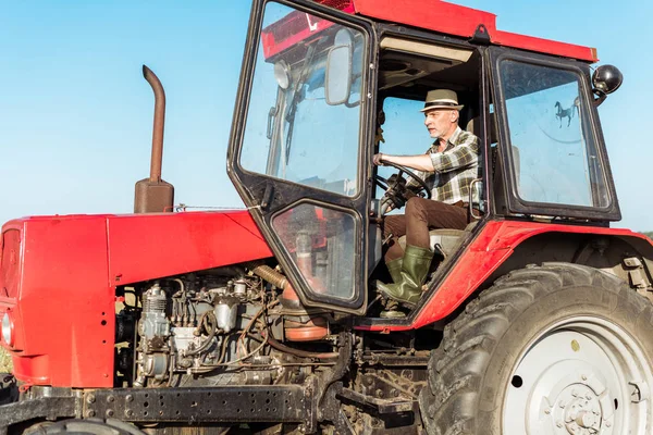 Agriculteur âgé conduisant tracteur moderne et rouge — Photo de stock