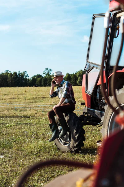 Selektiver Fokus des bärtigen Agronomen, der in der Nähe eines Traktors mit dem Smartphone spricht — Stockfoto